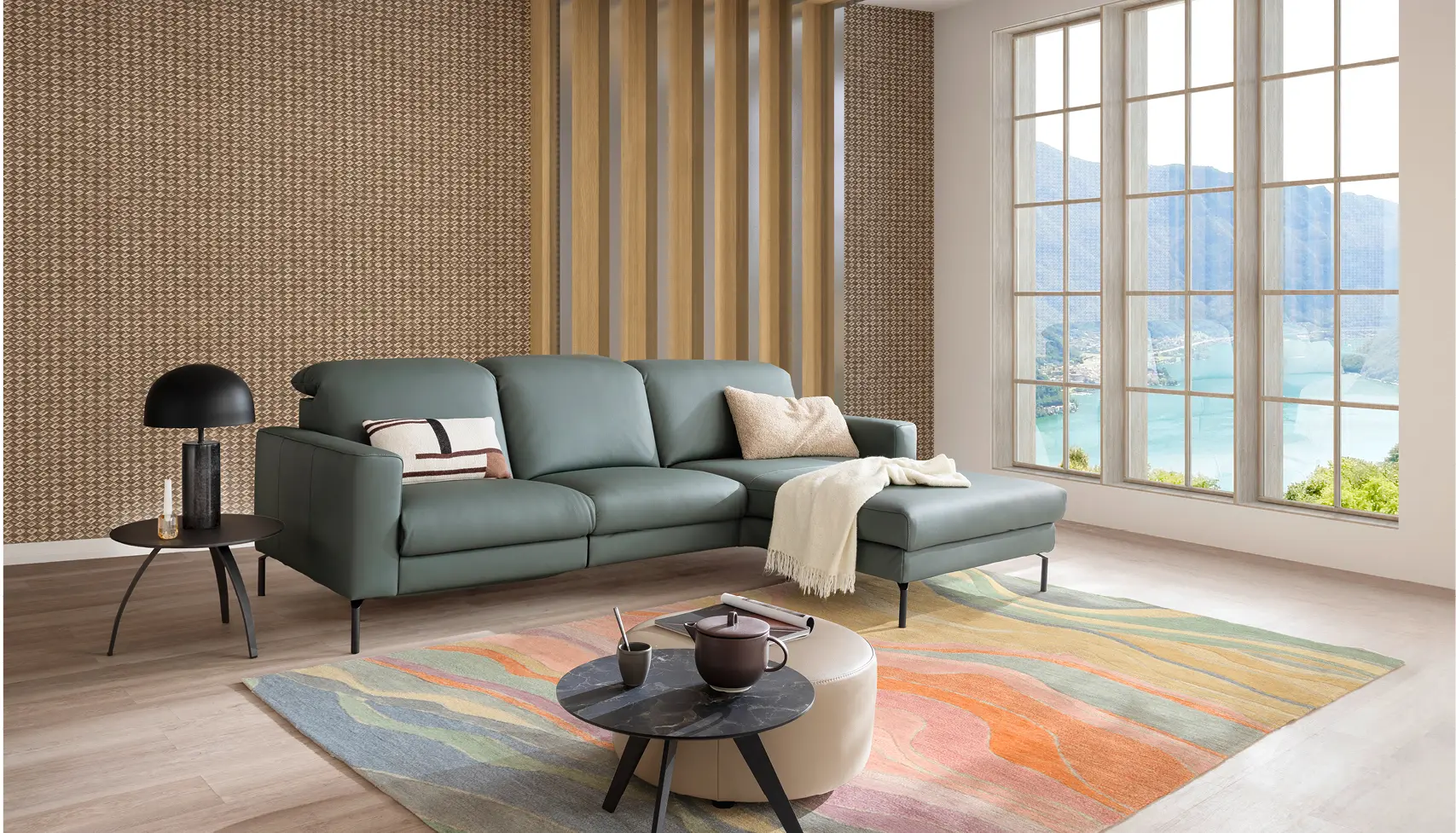 Helles Wohnzimmer mit grauem Ecksofa und Relaxsessel, dekoriert mit bunten Kissen, Pflanzen und Teppich im skandinavischen Stil – modernes Sofa-Design für gemütliches Wohnen.